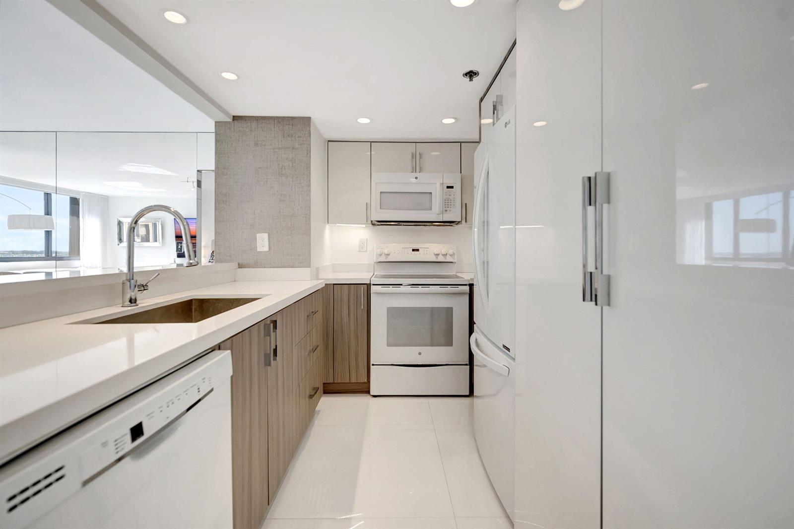 A modern kitchen features white countertops, wood-toned cabinetry, white appliances, and a pass-through window — 540 Brickell Key Drive # 919, Miami FL 33131, MIAMI, FL
