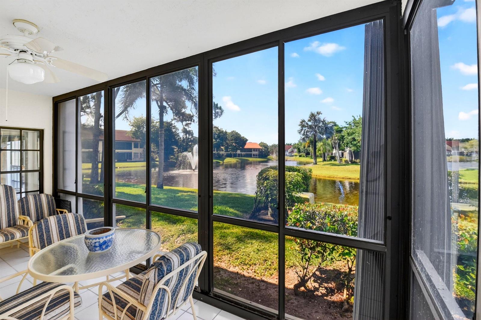A screened-in patio features striped chairs, a glass table, and a view of a pond — 3281 Jog Park Drive, FL 33467, FL