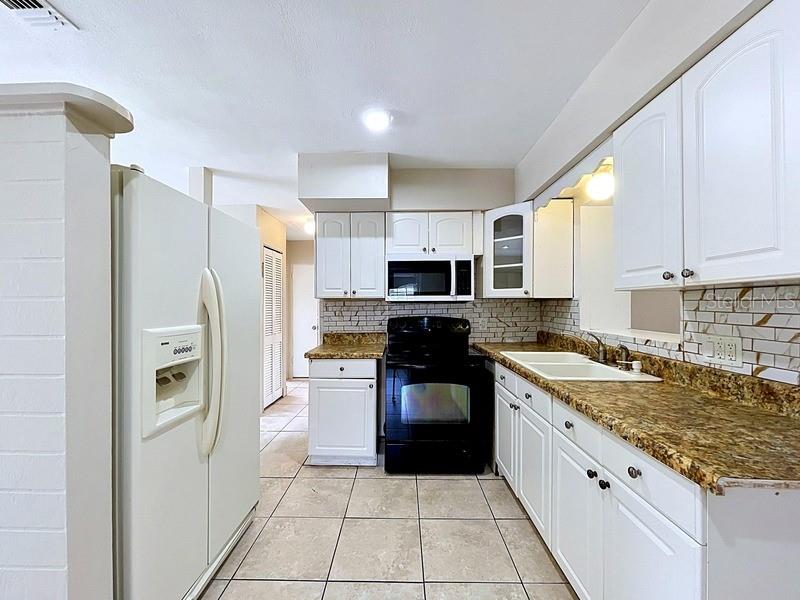 A kitchen features white cabinets, a black stove, a white refrigerator, and tan tile flooring — 7018 54TH AVENUE N, ST PETERSBURG, FL