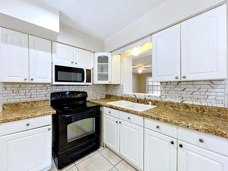 A kitchen features white cabinets, granite countertops, a black stove, and a subway tile backsplash — 7018 54TH AVENUE N, ST PETERSBURG, FL