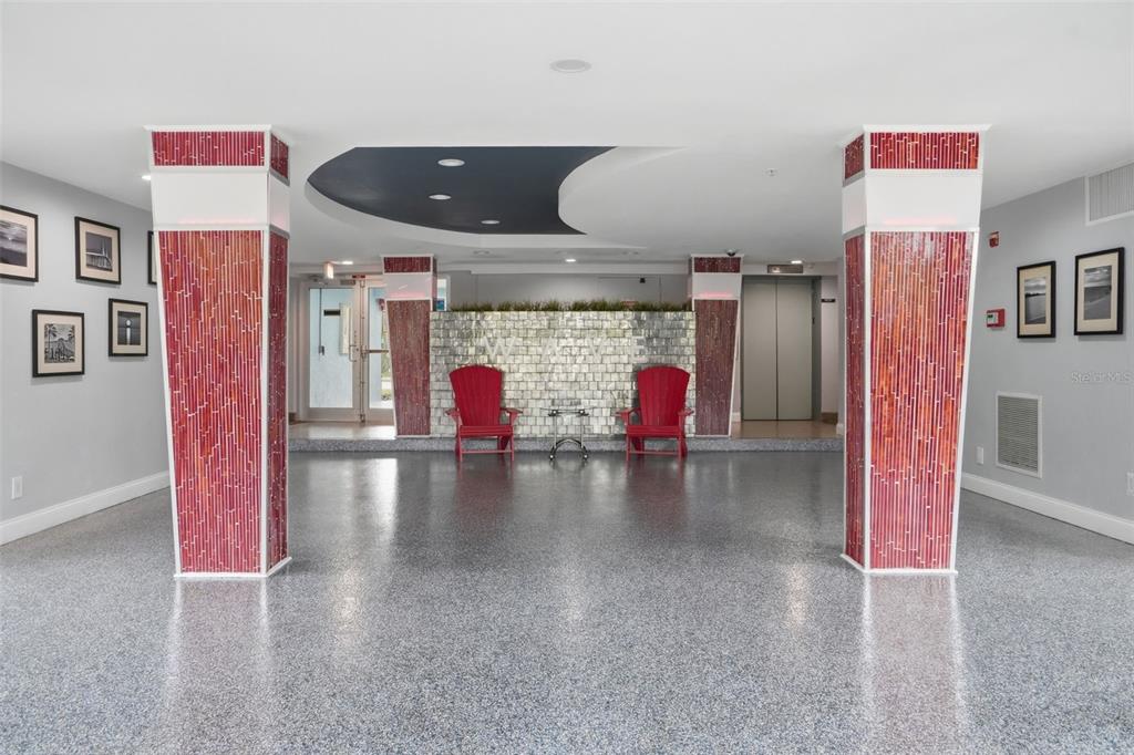 A modern building lobby features two red chairs, a tiled accent wall, and two decorative pillars — 3315 58TH AVENUE S UNIT 617, ST PETERSBURG, FL