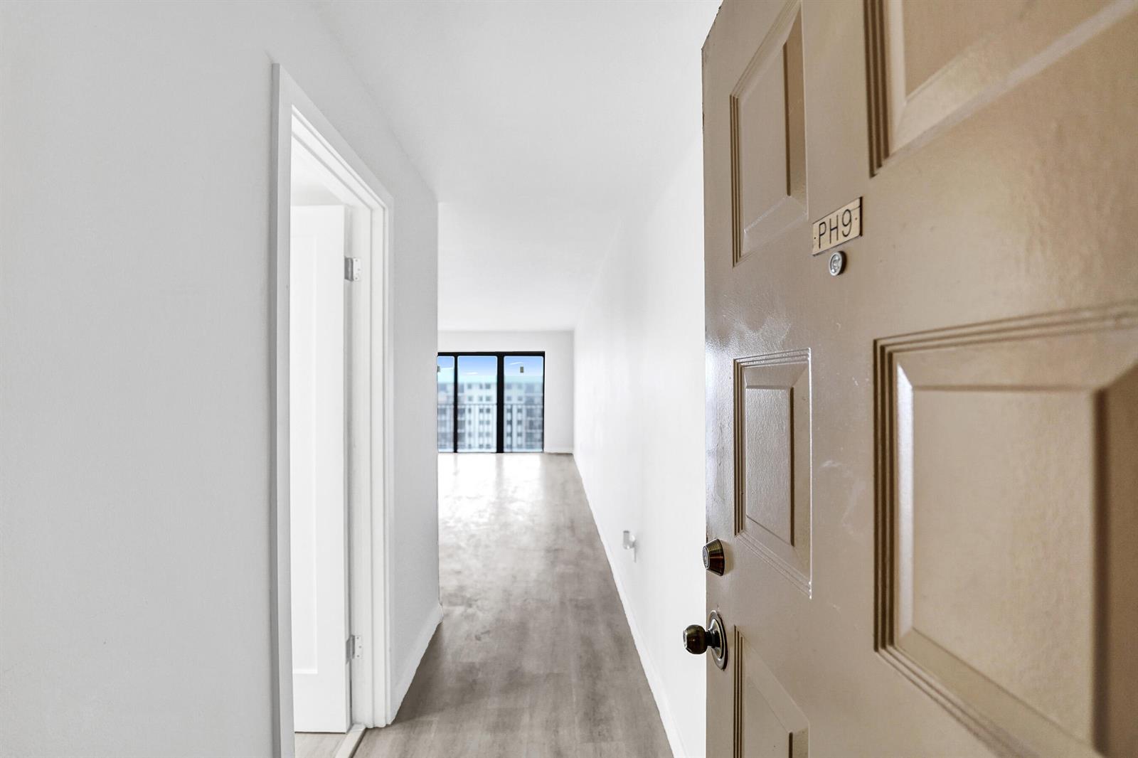 A view from an open doorway looking down a hallway toward a windowed living area — 1201 S Ocean Drive # 2509s, Hollywood FL 33019, HOLLYWOOD, FL