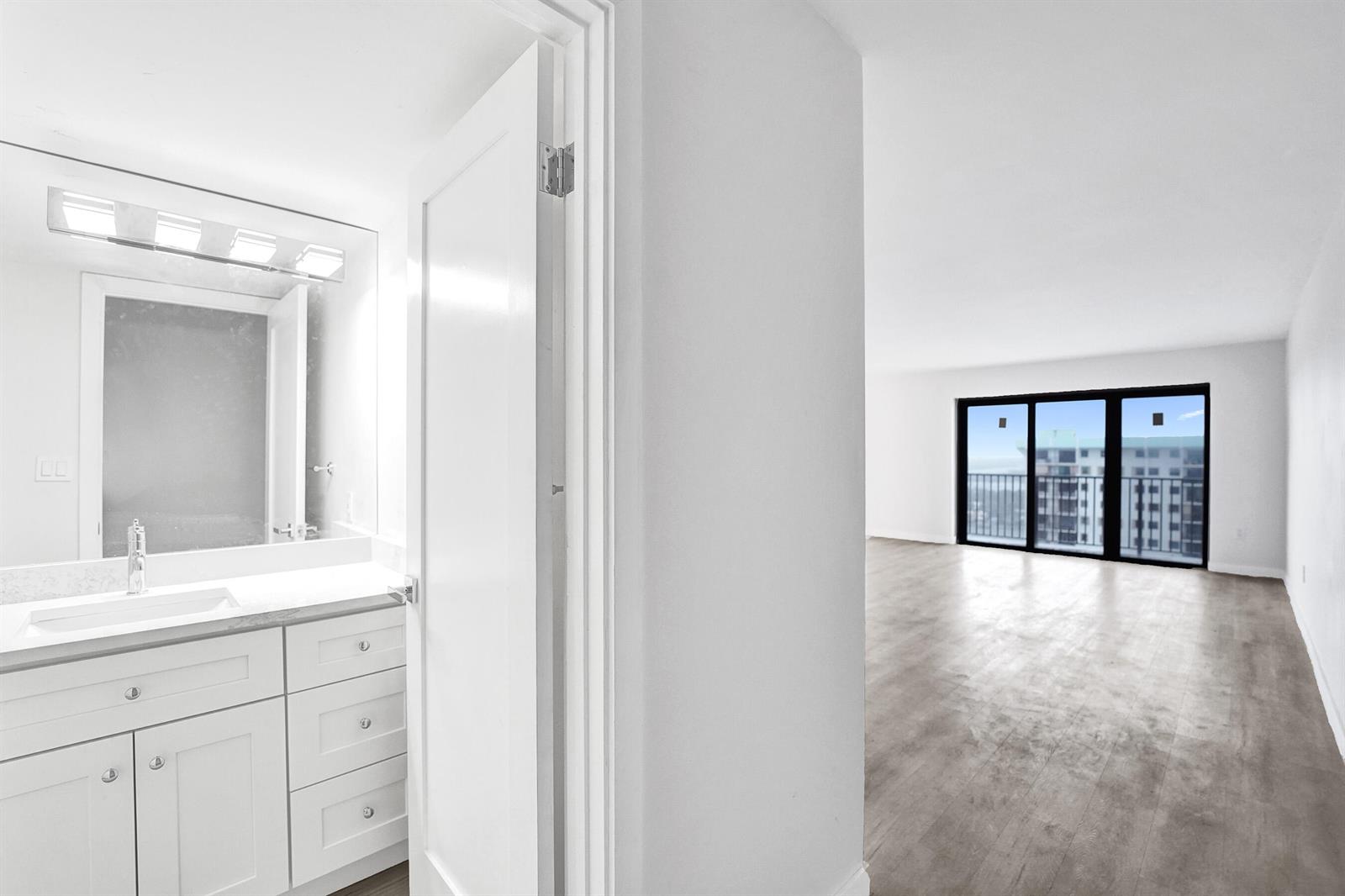 A white bathroom vanity sits next to a doorway opening into a bright, empty room — 1201 S Ocean Drive # 2509s, Hollywood FL 33019, HOLLYWOOD, FL