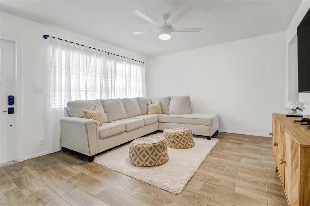A living room features a beige sectional sofa, two patterned ottomans, and wood-look tile flooring — 4711 FOREST GLEN DRIVE, NORTH FORT MYERS, FL
