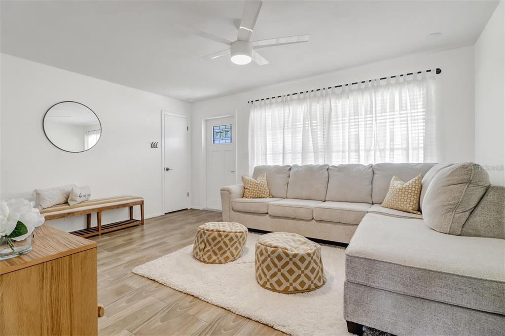 A living room features a light-colored sectional sofa, two patterned ottomans, and wood-look flooring — 4711 FOREST GLEN DRIVE, NORTH FORT MYERS, FL