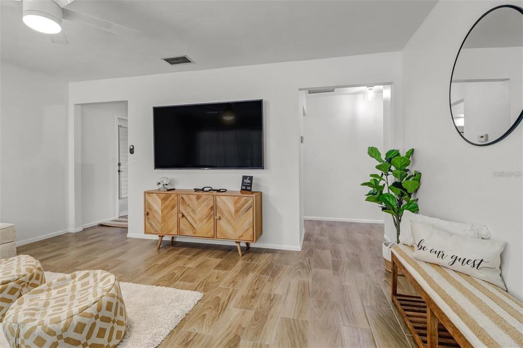 A living room features a wall-mounted television, a wooden media console, and wood-look flooring — 4711 FOREST GLEN DRIVE, NORTH FORT MYERS, FL