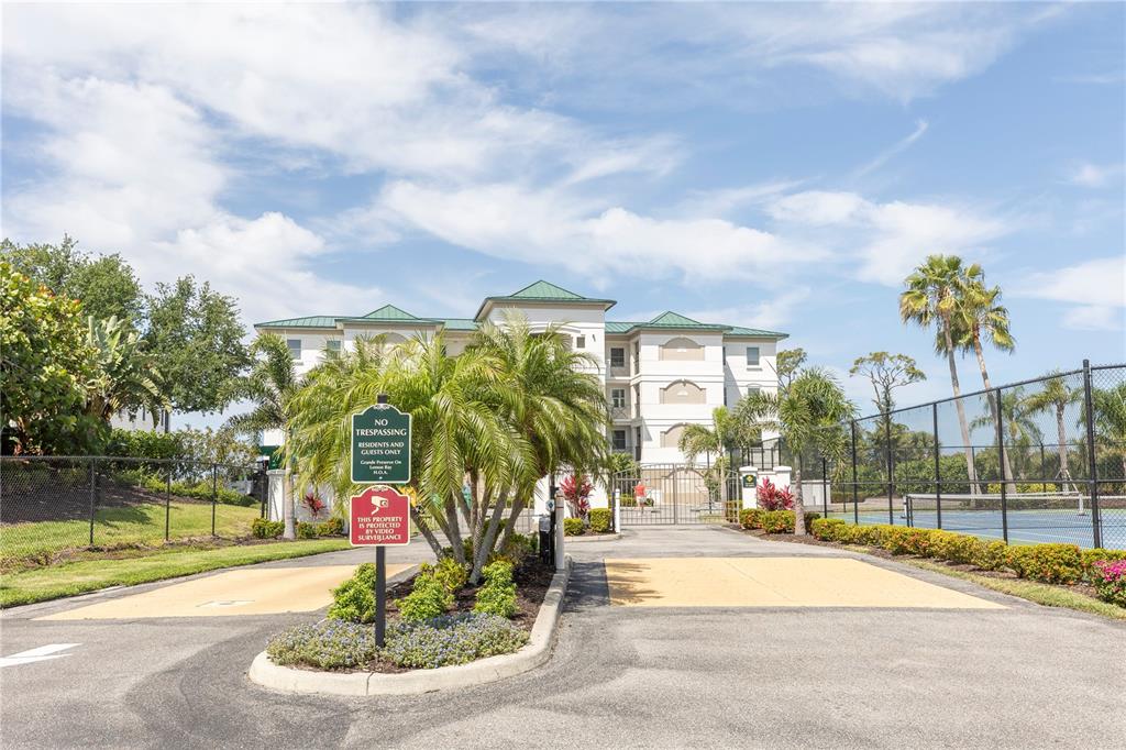 A multi-story apartment building stands behind a gated entrance with palm trees and tennis courts — 9203 GRIGGS ROAD UNIT D302, ENGLEWOOD, FL