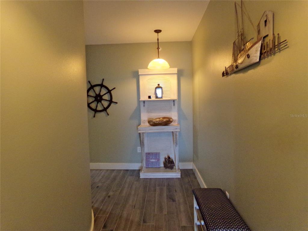 A hallway features wood-look flooring, a nautical-themed display shelf, and a decorative ship wall hanging — 9203 GRIGGS ROAD UNIT D302, ENGLEWOOD, FL