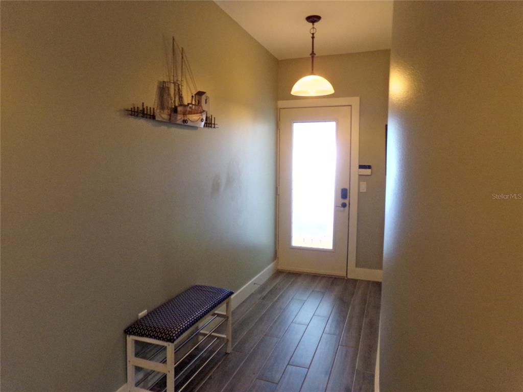An entryway features wood-look tile flooring, a bench, a wall-mounted ship model, and a pendant light — 9203 GRIGGS ROAD UNIT D302, ENGLEWOOD, FL