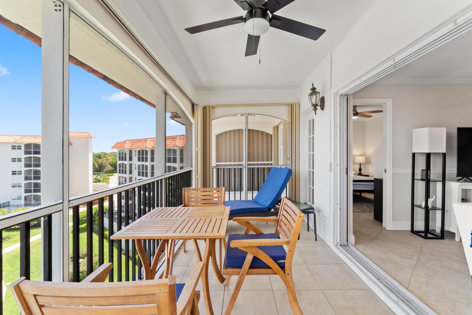 A screened-in balcony features a wooden table, chairs, a lounge chair, and tile flooring — 2871 N Ocean Boulevard # M538, Boca Raton FL 33431, BOCA RATON, FL