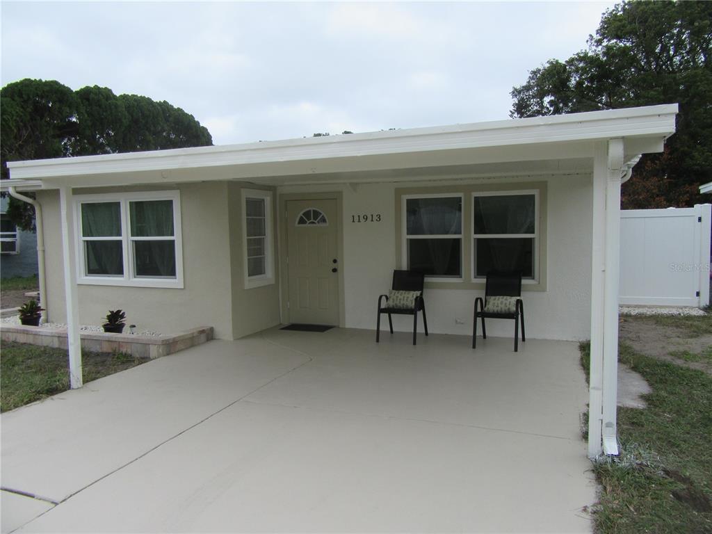 A single-story house exterior features a covered concrete carport, a front door, and two chairs — 11913 104TH STREET, LARGO, FL
