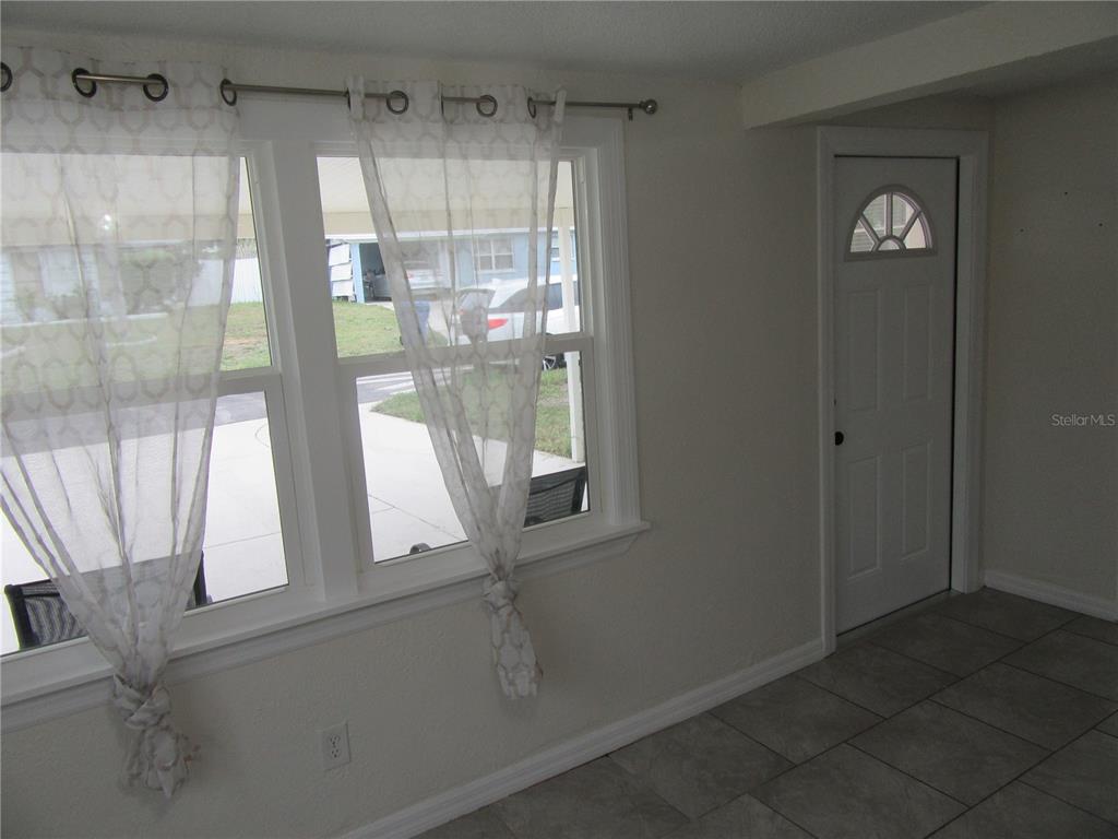 A room with light gray walls, tiled floors, white windows with sheer curtains, and a door — 11913 104TH STREET, LARGO, FL
