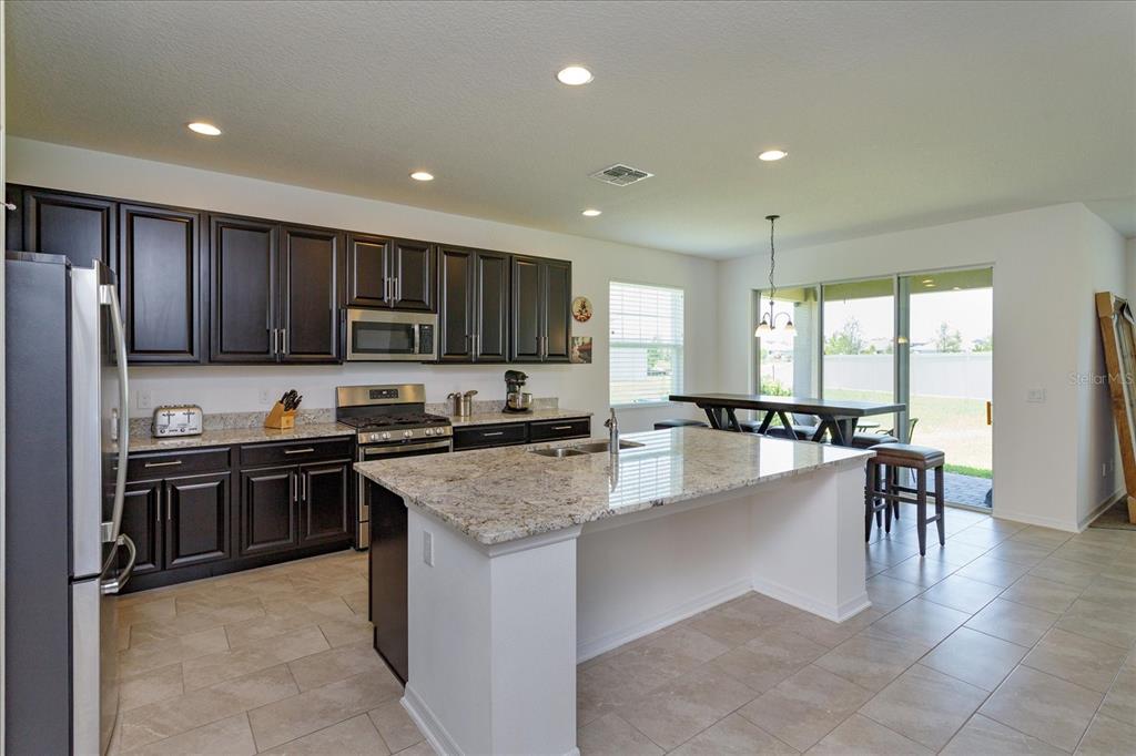 A kitchen features dark wood cabinets, granite countertops, a center island, and tile flooring — 16707 SANCTUARY DRIVE, WINTER GARDEN, FL