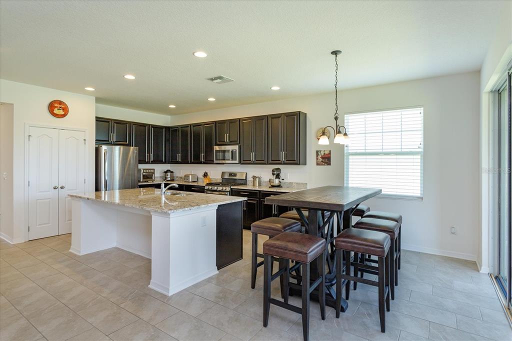 A kitchen features dark wood cabinets, granite countertops, a center island, and a dining table — 16707 SANCTUARY DRIVE, WINTER GARDEN, FL