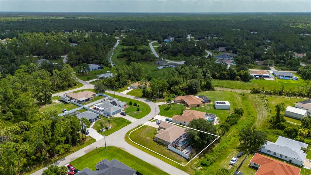 An aerial view shows a residential house with a pool cage and surrounding wooded lots — 5615 MOJAVE AVENUE, NORTH PORT, FL