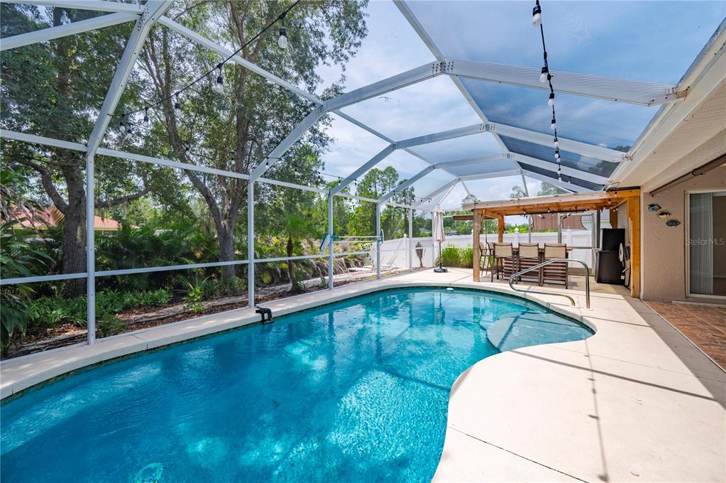 A screened-in swimming pool with a patio and a wooden pergola in a backyard — 5615 MOJAVE AVENUE, NORTH PORT, FL