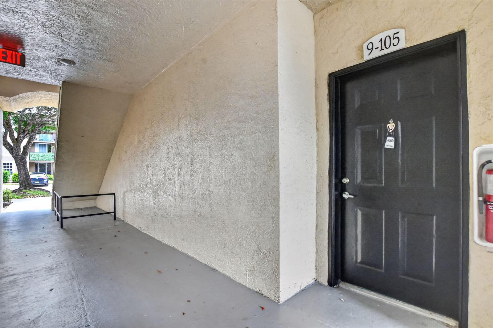 A dark door labeled 9-105 is located in a covered outdoor walkway with stucco walls — 15085 Michelangelo Boulevard # 105, Delray Beach FL 33446, DELRAY BEACH, FL