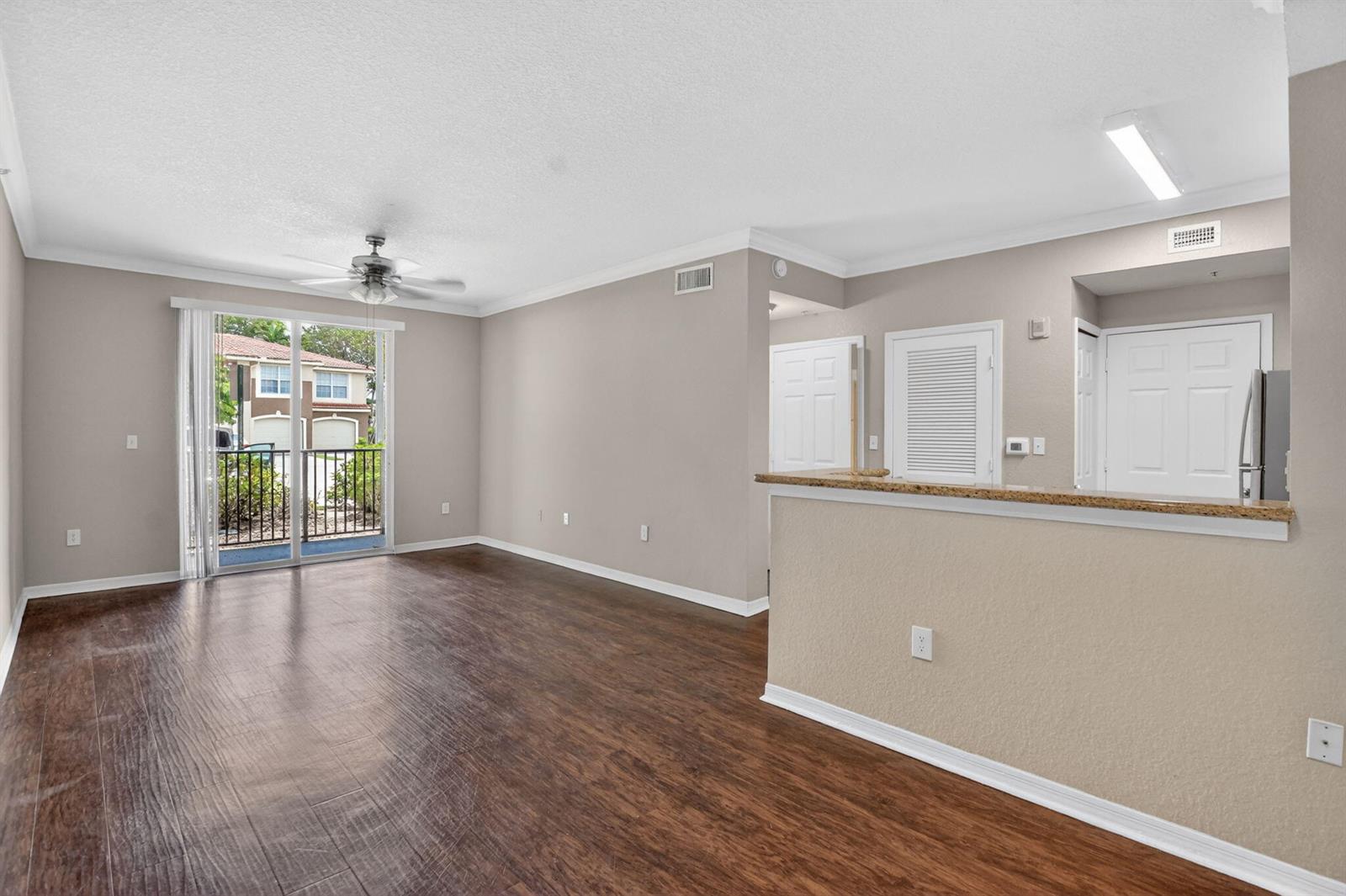 An empty living room with wood-look flooring, a ceiling fan, and a sliding glass door — 15085 Michelangelo Boulevard # 105, Delray Beach FL 33446, DELRAY BEACH, FL
