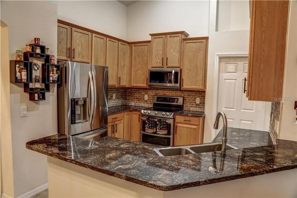 A kitchen features oak cabinets, dark granite countertops, stainless steel appliances, and a tile backsplash — 1521 ECHO LAKE COURT, ORLANDO, FL