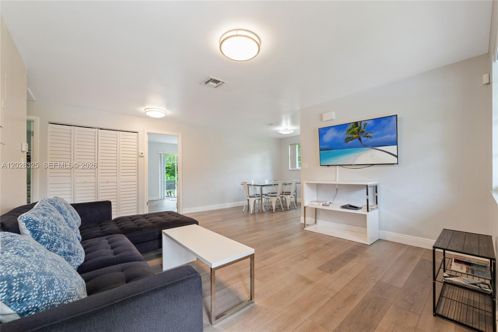 A living room with a dark sectional sofa, a wall-mounted television, and a dining area — 6198 SW 63rd St, South Miami FL 33143, SOUTH MIAMI, FL
