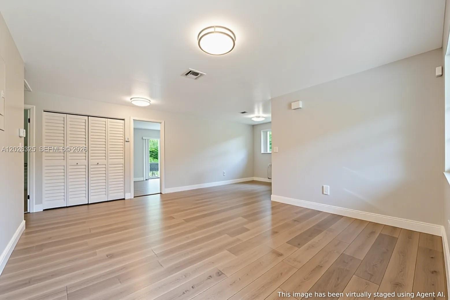An empty room features light wood-look flooring, white walls, and white louvered closet doors — 6198 SW 63rd St, South Miami FL 33143, SOUTH MIAMI, FL