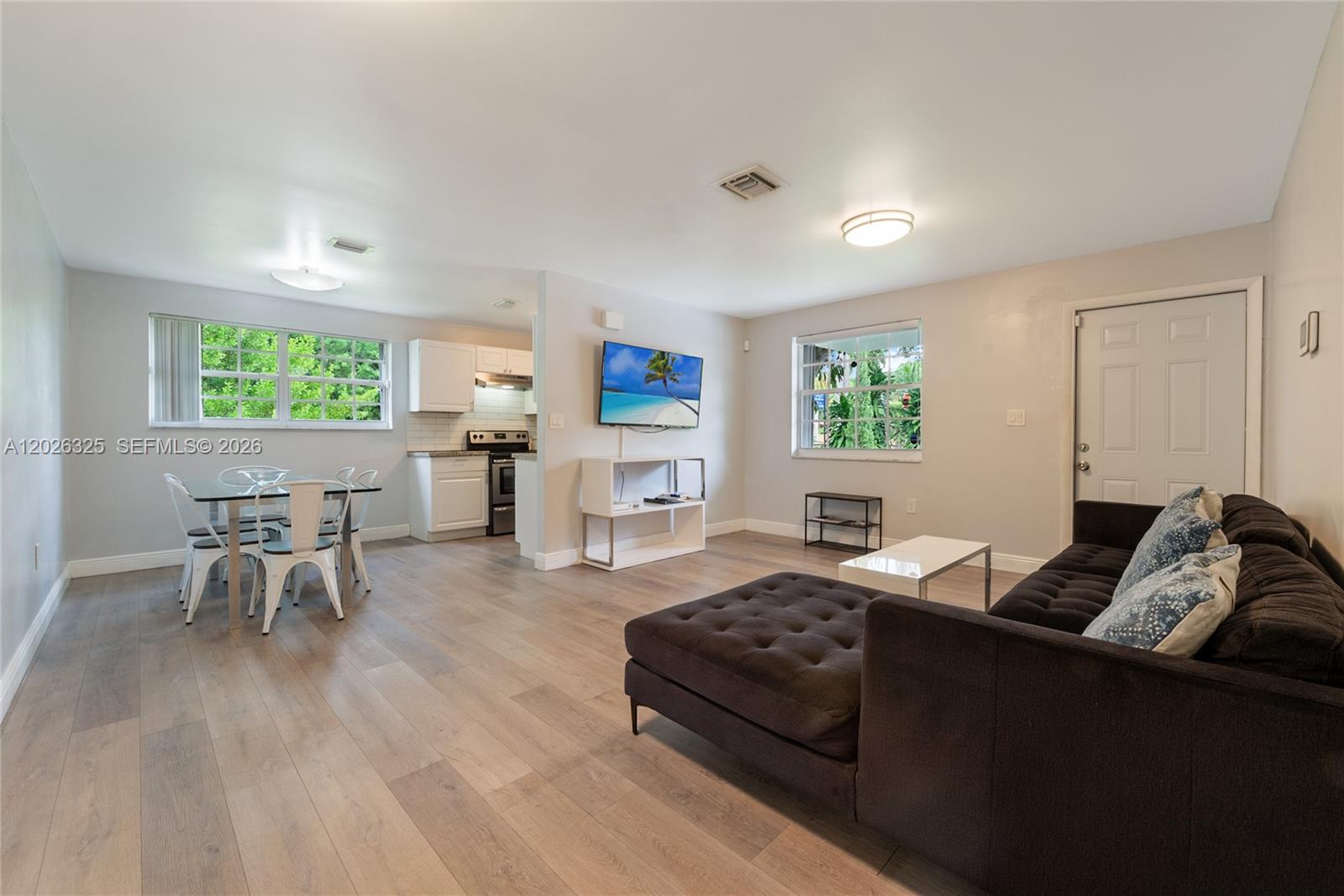 This open-concept living and dining area features light wood flooring and a modern kitchen — 6198 SW 63rd St, South Miami FL 33143, SOUTH MIAMI, FL