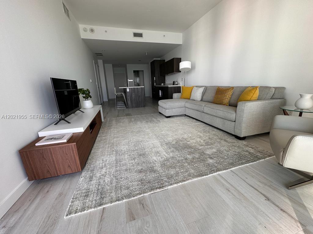 A modern living room features a grey sectional sofa, a large area rug, and wood cabinetry — 480 NE 31st St # 1902, Miami FL 33137, MIAMI, FL