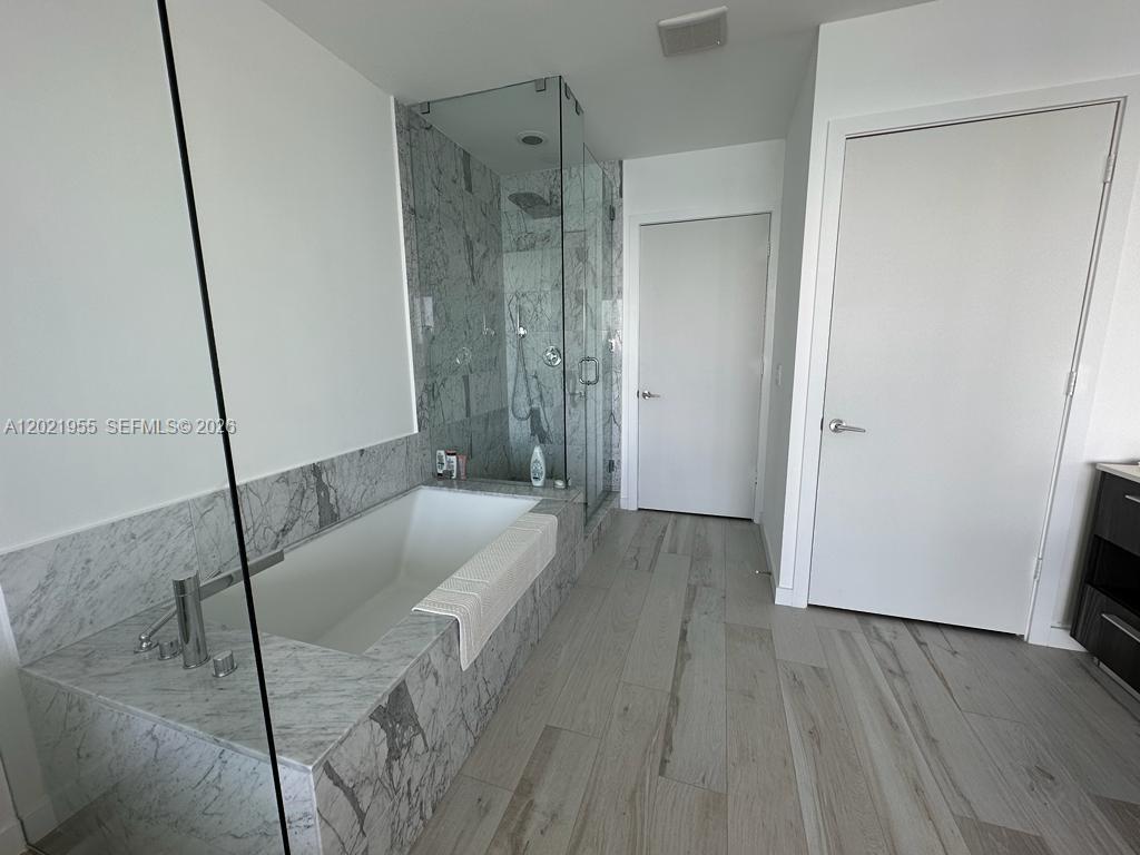 A modern bathroom features a marble-tiled soaking tub, a glass-enclosed shower, and wood-look tile flooring — 480 NE 31st St # 1902, Miami FL 33137, MIAMI, FL
