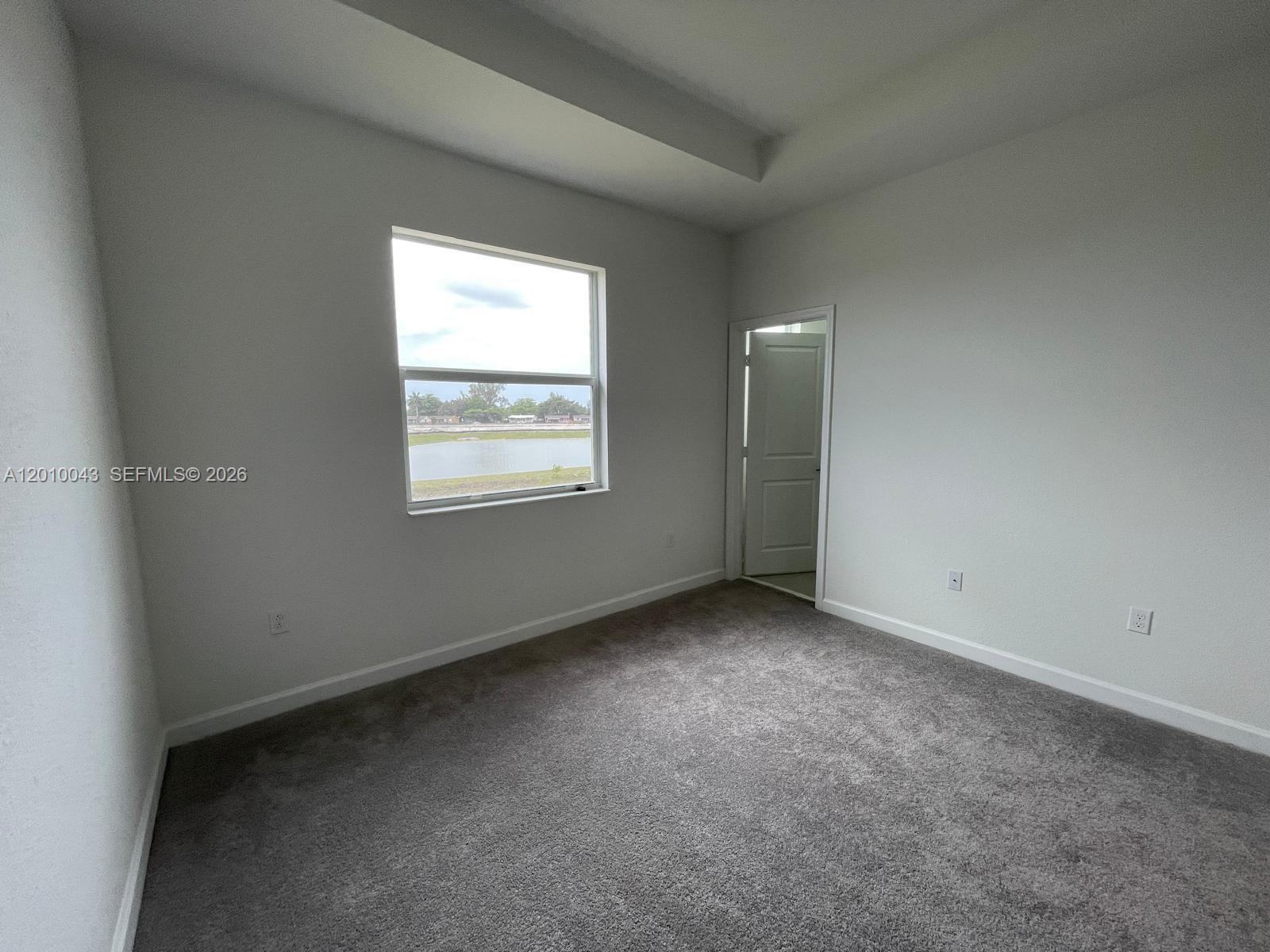 An empty bedroom features gray carpet, white walls, a tray ceiling, and a window view — 12372 NW 23rd Ct # 12372, Miami FL 33167, MIAMI, FL