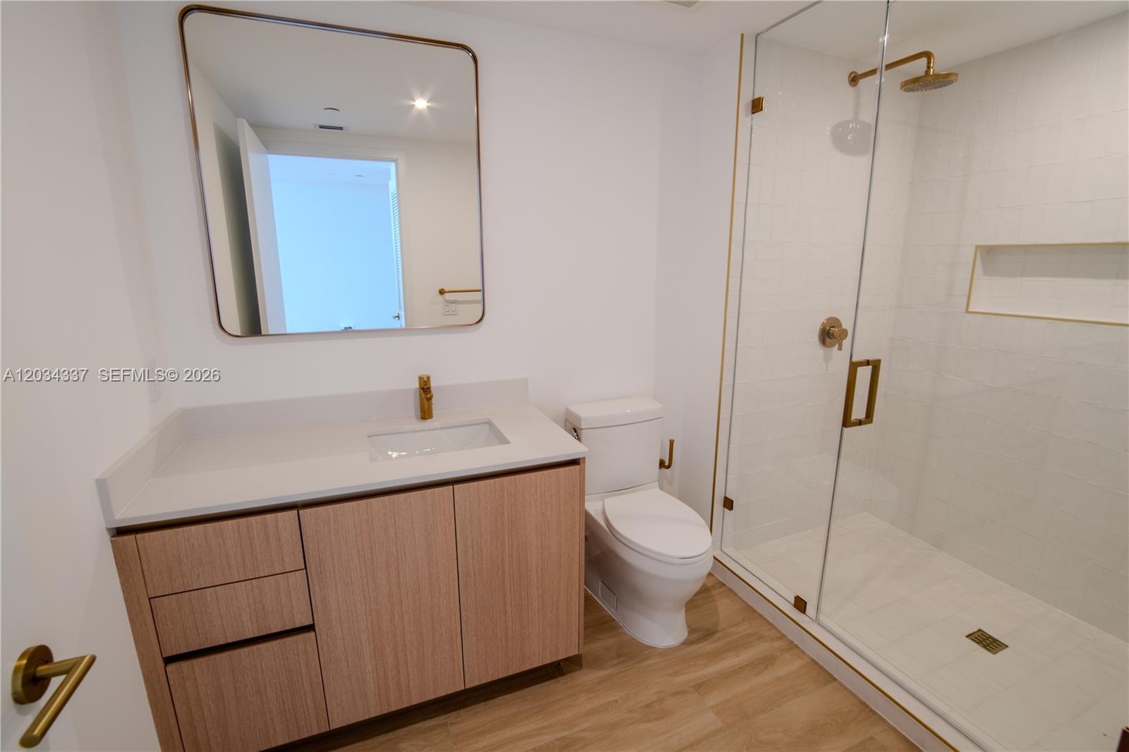 A modern bathroom features a light wood vanity, white countertop, gold fixtures, and glass shower — 90 NE 32nd St # 824, Miami FL 33137, MIAMI, FL