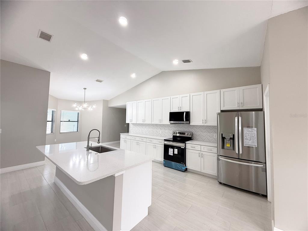 A modern kitchen features white cabinetry, stainless steel appliances, a large island, and tile flooring — 4548 YORKSHIRE LANE, KISSIMMEE, FL