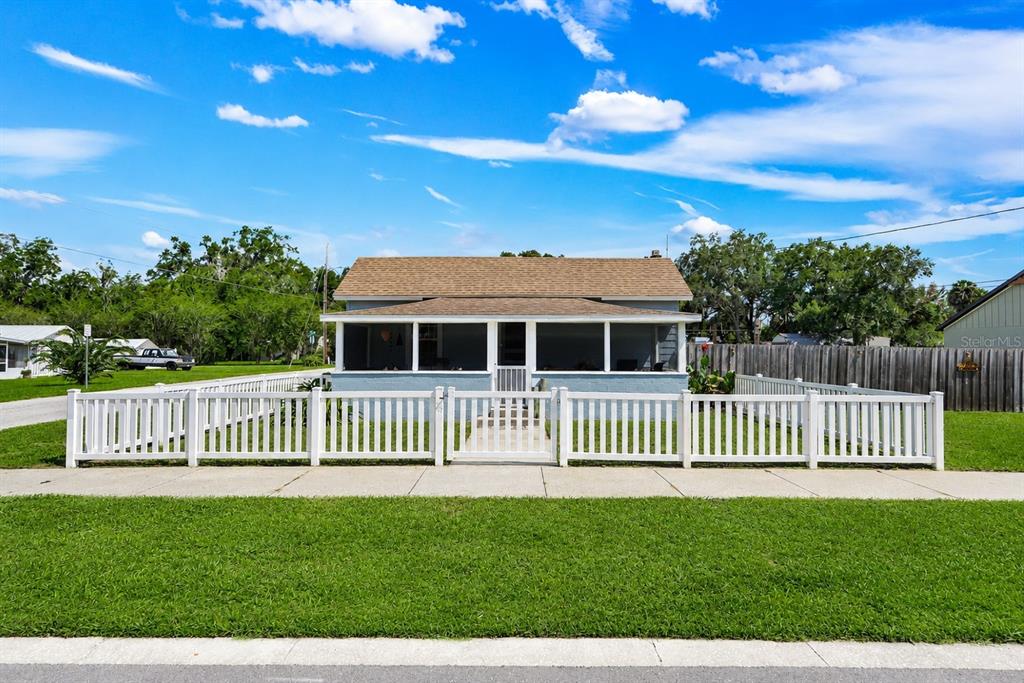 A single-story house with a screened front porch sits behind a white picket fence — 321 CASSADY STREET, UMATILLA, FL