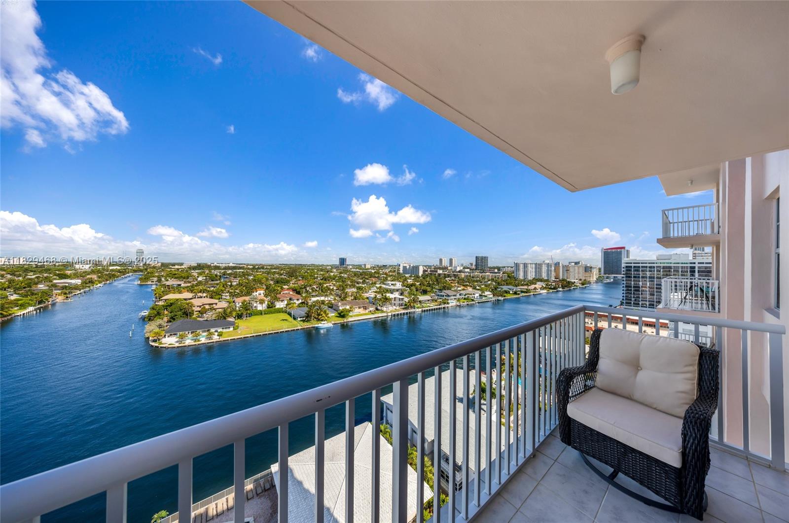 A balcony with a wicker chair overlooks a canal and residential neighborhood under a blue sky — 3161 S Ocean Dr # 1510, Hallandale Beach FL 33009, HALLANDALE BEACH, FL