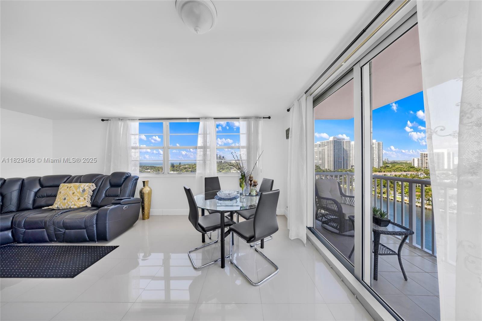 A bright living and dining area features white tile floors, a dark sofa, and balcony access — 3161 S Ocean Dr # 1510, Hallandale Beach FL 33009, HALLANDALE BEACH, FL