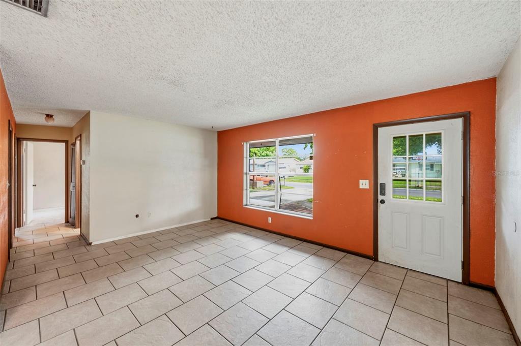 A living room with light tile flooring, a textured ceiling, and a bright orange accent wall — 8168 82ND AVENUE, SEMINOLE, FL