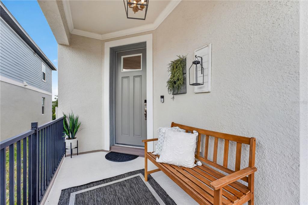 A covered porch features a gray front door, a wooden bench, and a black railing — 2326 RAVEN RIDGE ROAD, MINNEOLA, FL