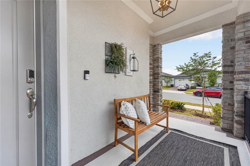 A covered front porch features a wooden bench, a rug, and stone-accented columns — 2326 RAVEN RIDGE ROAD, MINNEOLA, FL