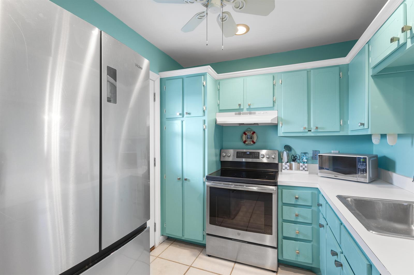 A kitchen features turquoise cabinets, stainless steel appliances, and white countertops — 3851 N Ocean Boulevard Unit 404, Delray Beach FL 33483, DELRAY BEACH, FL