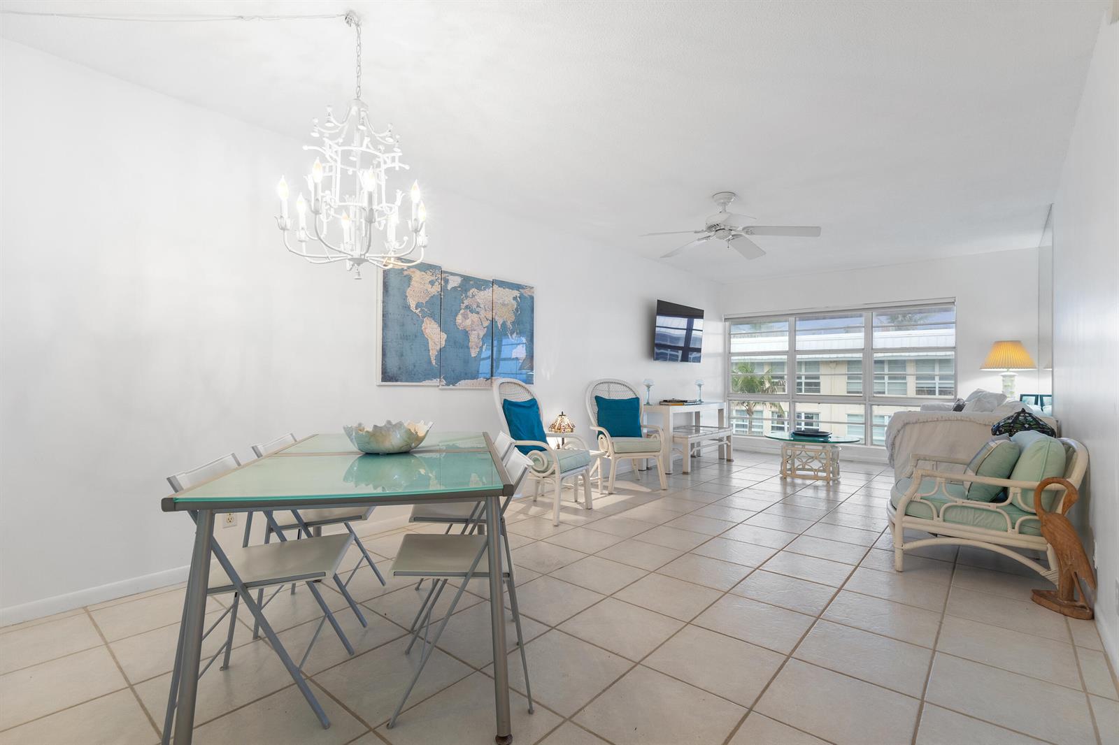 A bright, open-concept living and dining area features white tile floors and a glass-topped table — 3851 N Ocean Boulevard Unit 404, Delray Beach FL 33483, DELRAY BEACH, FL