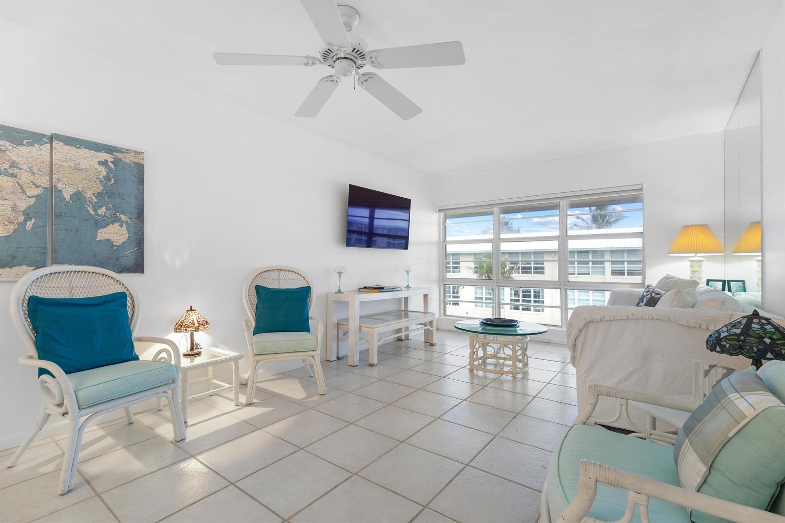 A bright living room features white tile floors, wicker furniture, and a large wall map — 3851 N Ocean Boulevard Unit 404, Delray Beach FL 33483, DELRAY BEACH, FL
