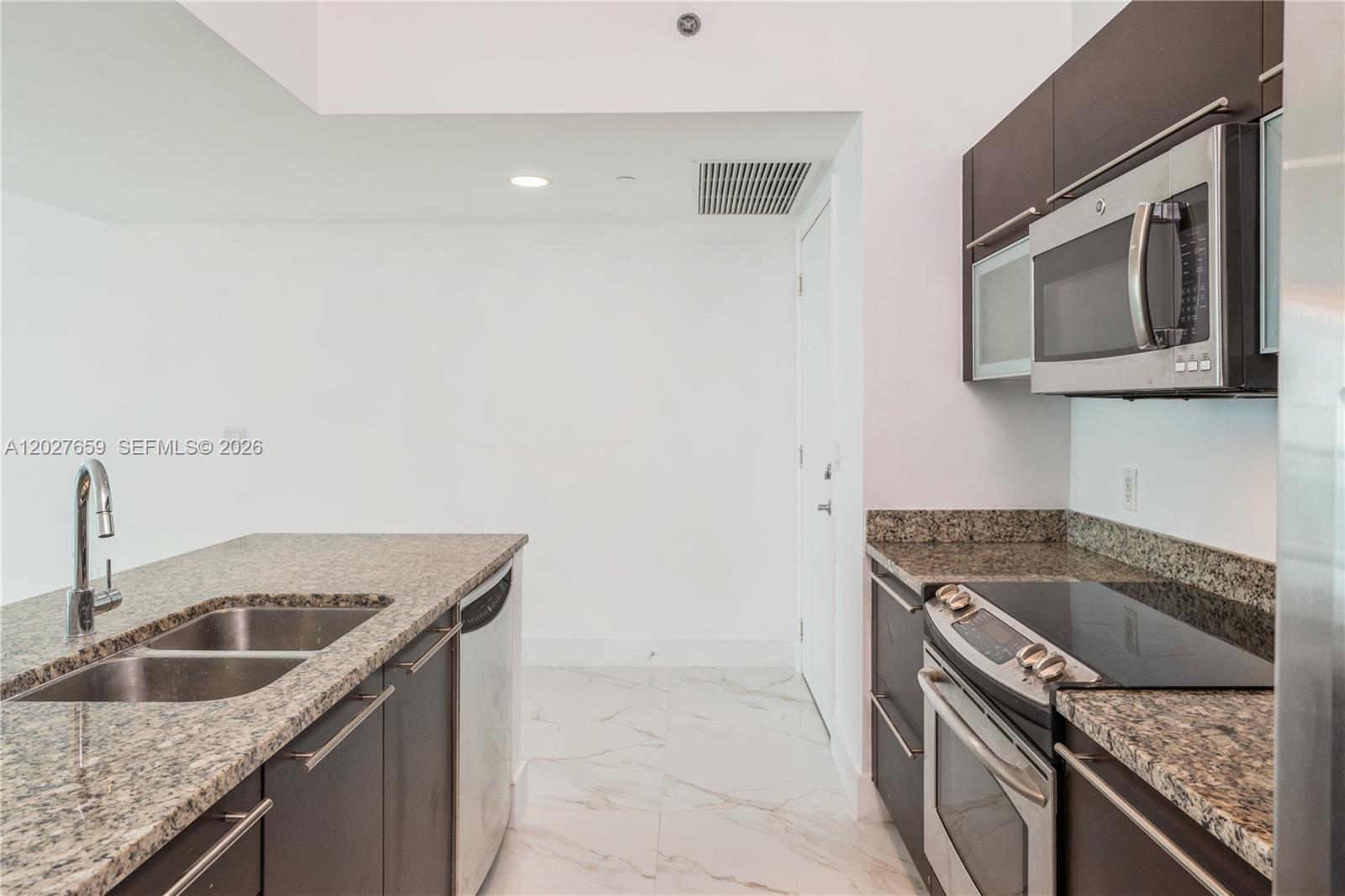 A modern kitchen features dark cabinetry, granite countertops, stainless steel appliances, and white marble flooring — 951 Brickell Ave # 3706, Miami FL 33131, MIAMI, FL