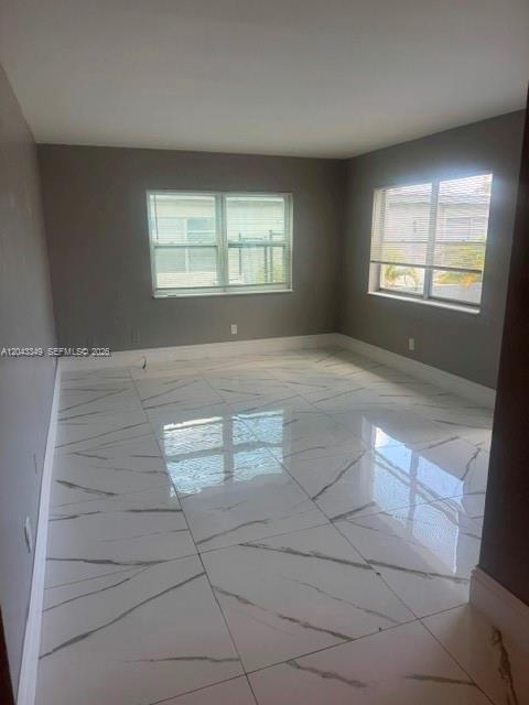 An empty room features gray walls, white baseboards, and large white marble-patterned floor tiles — FORT LAUDERDALE, FL