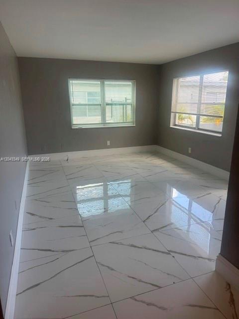 An empty room features gray walls, white baseboards, and large white marble-patterned floor tiles — FORT LAUDERDALE, FL