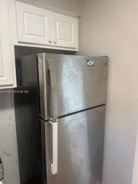 A stainless steel top-freezer refrigerator is positioned beneath white kitchen cabinets against a gray wall — FORT LAUDERDALE, FL