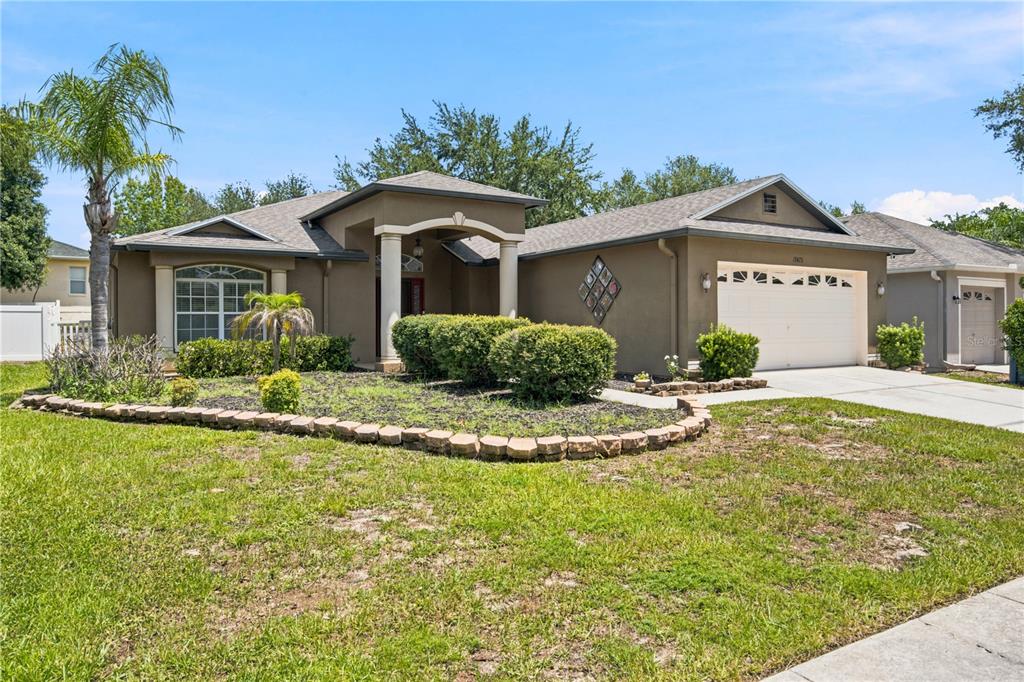 A single-story tan house with a two-car garage, arched entryway, and landscaped front yard — 13475 TEABERRY LANE, SPRING HILL, FL