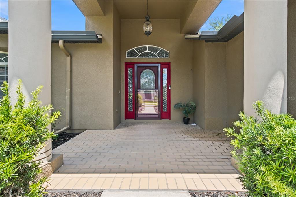 A covered entryway features a red front door, a brick-paved porch, and two large columns — 13475 TEABERRY LANE, SPRING HILL, FL