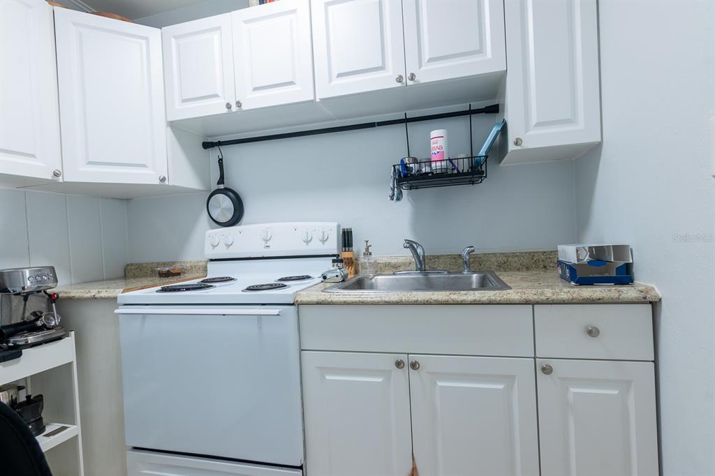 A small kitchen features white cabinets, a white electric stove, and a stainless steel sink — 610 N EAST AVENUE, SARASOTA, FL