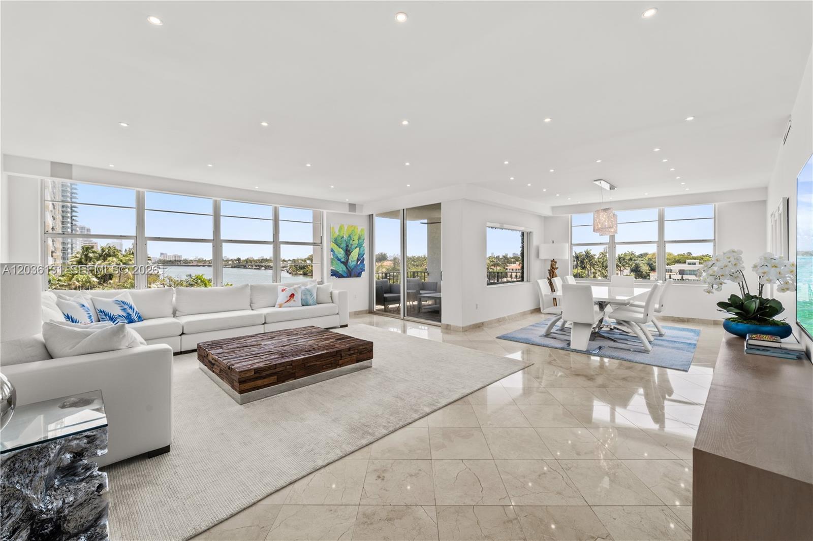 A bright, open-concept living and dining area features white furniture, tile floors, and waterfront views — 5640 Collins Ave # 4D, Miami Beach FL 33140, MIAMI BEACH, FL