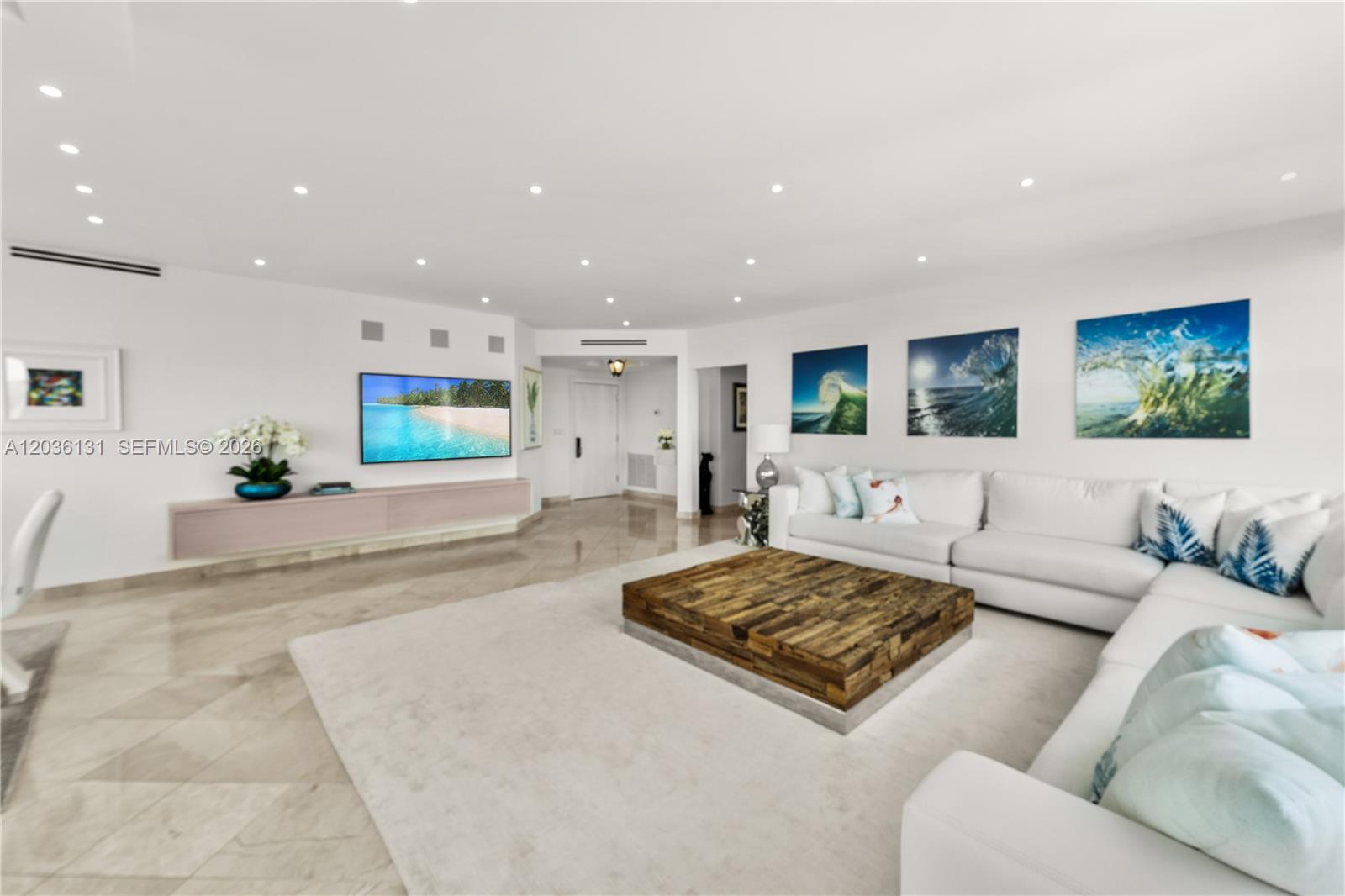 A spacious living room features a large white sectional sofa, wooden coffee table, and television — 5640 Collins Ave # 4D, Miami Beach FL 33140, MIAMI BEACH, FL