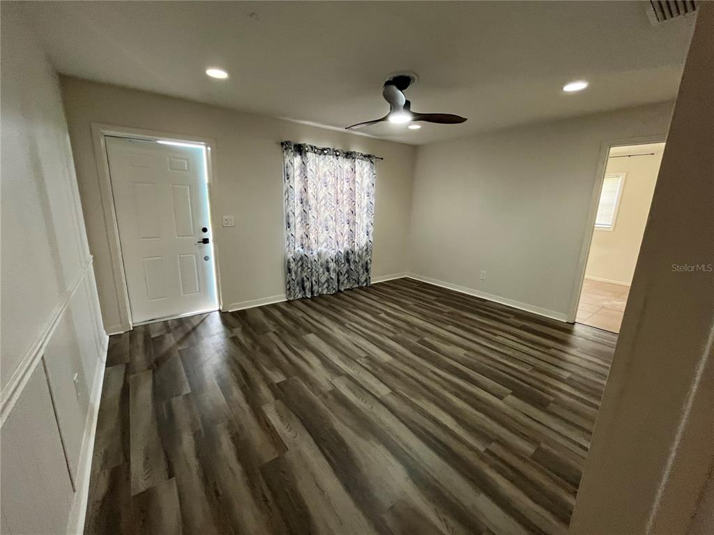 An empty room features wood-look flooring, a ceiling fan, and a white entry door — 6950 ROSEMONT DRIVE UNIT A&B, ENGLEWOOD, FL
